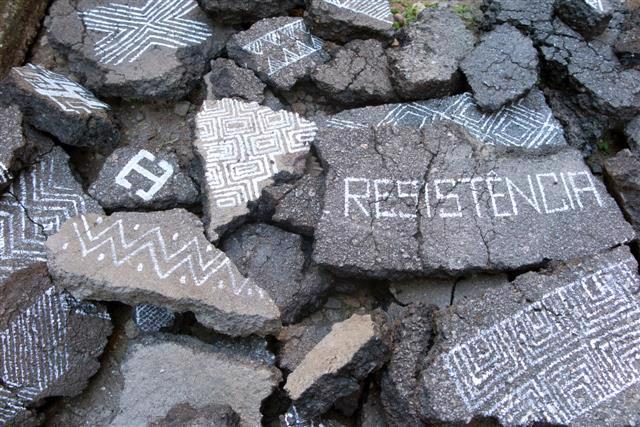 Fotografia de pedras partidas, com desenhos em branco de formas geométricas e a palavra RESISTÊNCIA.