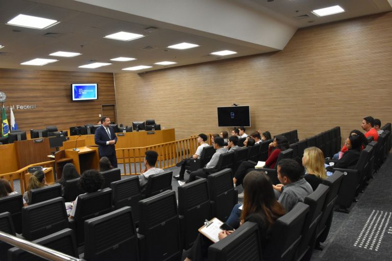 Em uma das salas onde ocorrem as sessões de julgamento, o juiz federal Fabrício Fernandes de Castro, em pé, discorre sobre a estrutura organizacional da Justiça Federal para os estudantes do CEL, sentados